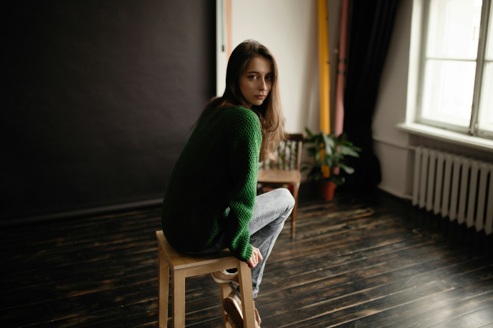 Photo d'une adolescente avec un gilet vert assise sur un tabouret et en manque d'estime d'elle-même